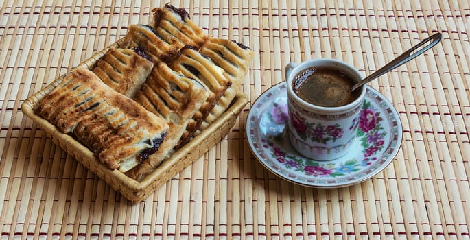A cup of fresh black coffee standing on a saucer and fresh puff with berries lie in a straw basket