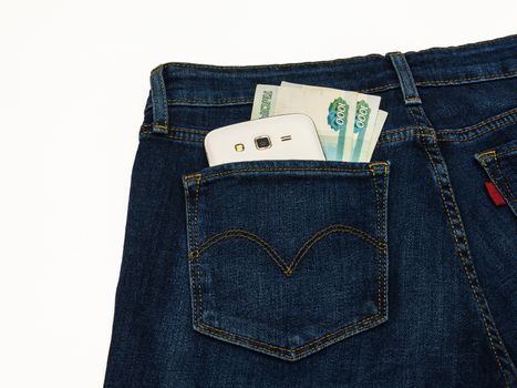 Trousers sewn from a blue denim lie on a white surface. In the back pocket of his pants is smart and banknotes.


