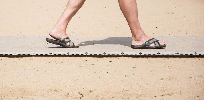 On the yellow sand beach lies on the path and there are feet in the summer slates
