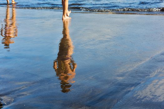 Two female figures are reflected in the wet sand prebrezhnogo