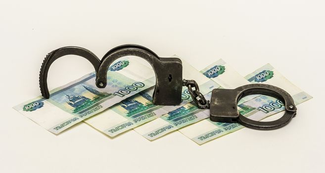 On a white background are banknotes 1000 Russian rubles. kupyurazh lie on black metal handcuffs.


