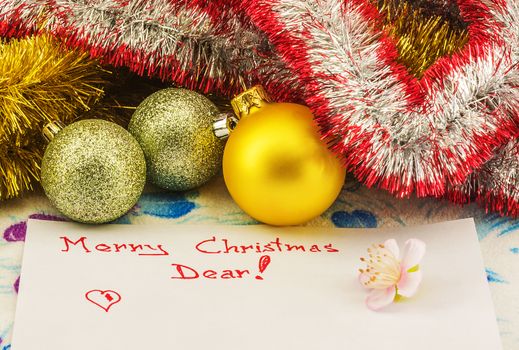 On a sheet of paper written with Christmas greetings. next to the sheet lying Christmas balls and meshura for decoration.