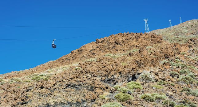 Blue cabin cable car with tourists climbing ropes stretched to the volcano Teide on Tenerife island.

