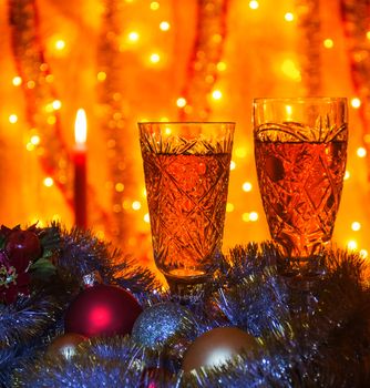 Some wine glasses of champagne lying Christmas balls and tinsel. On blurred background is visible burning candle.

