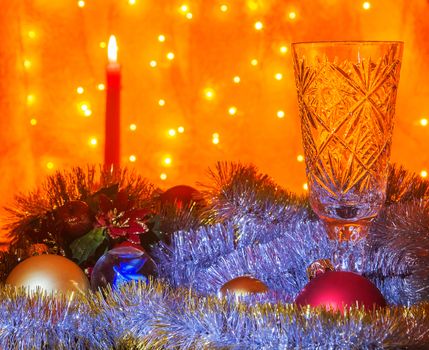 Next to empty a glass of champagne lying Christmas balls and tinsel. On blurred background is visible burning candle.

