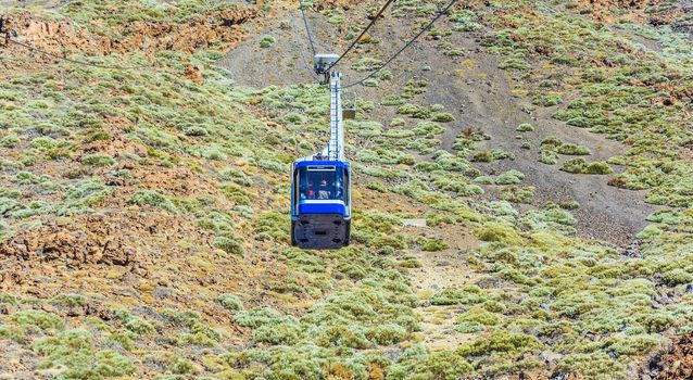 Blue cabin cable car with tourists climbing ropes stretched to the volcano Teide on Tenerife island.


