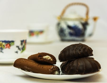 In the foreground are seen marshmallows and cookies with filling. On average, and further plans are visible mugs and tea makers, who do not have the sharpness.

