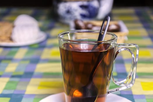 On a white saucer is a glass cup with tea and a metal spoon