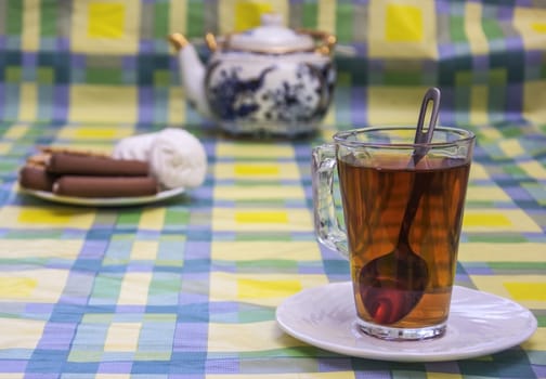 In the foreground is a white saucer glass cup of tea. In the background, without the sharpness seen tea and a bowl of sweets.