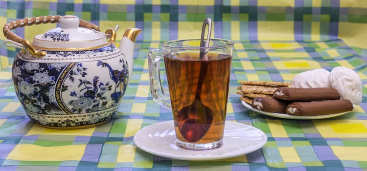 On the table is a glass cup with tea, tea and sweets in the basket are