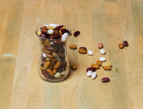 On a wooden surface is a glass beaker. In a glass sprinkled haricot beans. A few grains scattered nearby.
