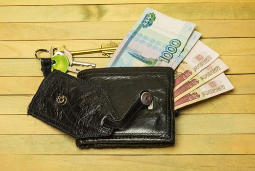 On a wooden surface lie the keys and unbuttoned the purse from which money can be seen euro banknotes
