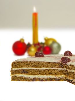 On a white background is clearly visible sponge layer cake. In the background a burning candle and festive balloons