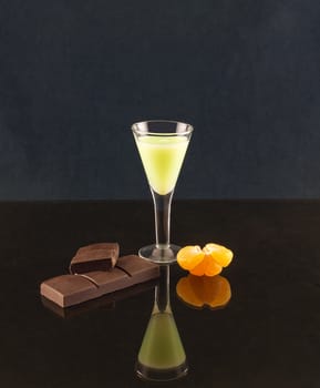 On the mirror surface reflects a glass with a drink, chocolate and half tangerine