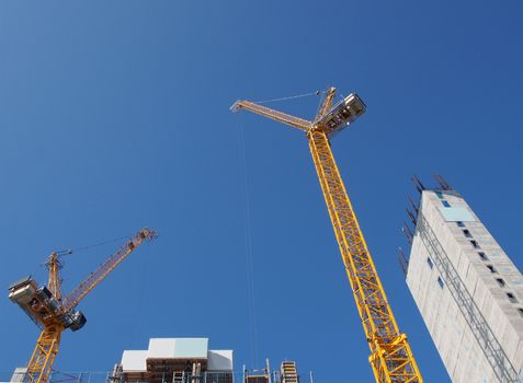 two tall yellow tower cranes working on a large residential construction site with a large concrete tower against a blue sky