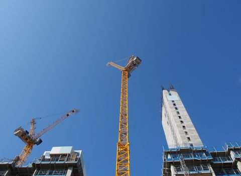 a view of tall tower cranes working on large construction sites against a blue sky in leeds england