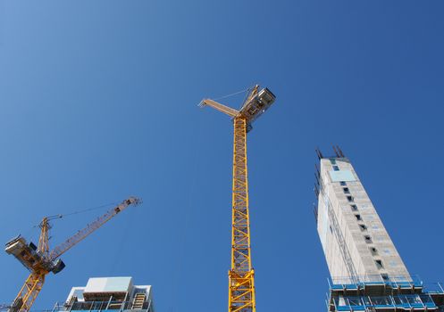 a view of tall tower cranes working on large construction sites against a blue sky in leeds england