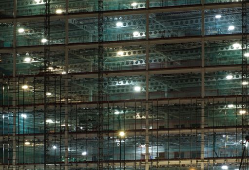 a full frame view of a large construction site at night illuminated by bright work lights with girders and construction hoists