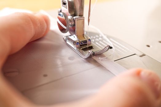 A woman works on a sewing machine. seamstress sews white curtains, close up view