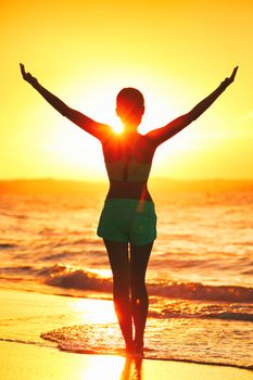 Wellness girl doing sun salutation morning yoga. Carefree person living a free life. Cheering woman open arms to sunrise on beach. Success freedom happiness concept.