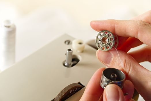 hands of a seamstress winding thread from a spool to a bobbin, close-up