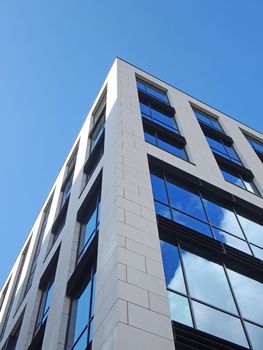 upwards view of the corner of a white modern office building with blue sky and clouds reflected in large glass windows