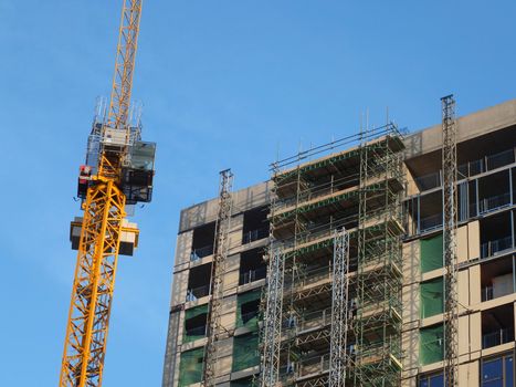 a yellow construction crane next to a large concrete building under construction with scaffolding and hoist towers