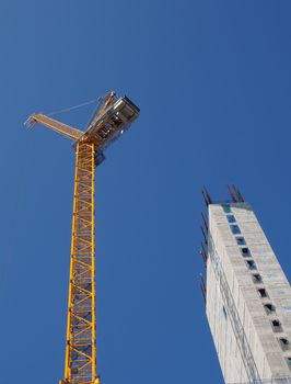 a yellow tower crane working on a construction site with a tall concrete building against a bright blue sky