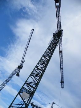 vertical view of tall tower cranes working on a large construction site against bright blue sky and clouds