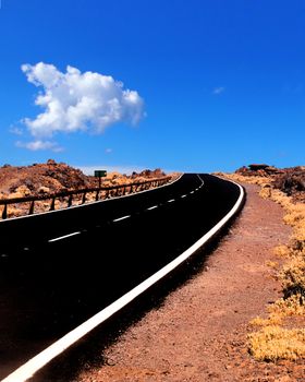 a long empty road stretching to the horizon with mountains in the background arid summer desert landscape and blue sunlit sky