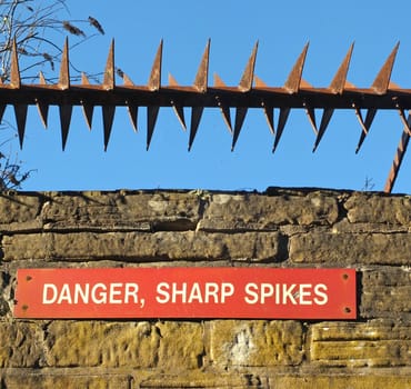 rusty iron sharp spikes on the top of an old stone wall with a red danger sign against a blue sky