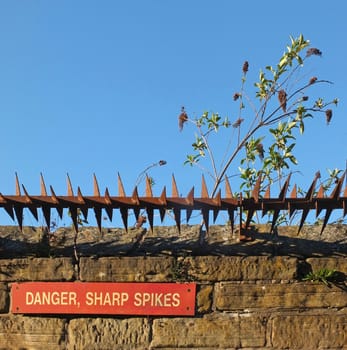 rusty iron sharp spikes on the top of an old stone wall with a red danger sign against a blue sky