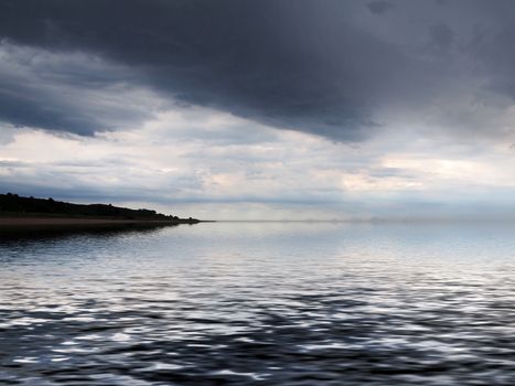 a distant coast reflected in the sea with dramatic dark storm clouds