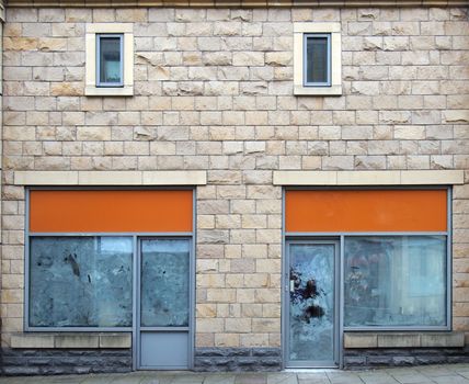 two empty abandoned shops on a street with whitewashed empty windows and blank store signs