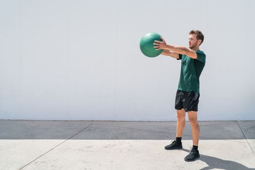 Medicine ball workout fitness man strength training arms doing deltoid front raise exercise for shoulder muscles. Upper body workout with weight ball at fitness centre.