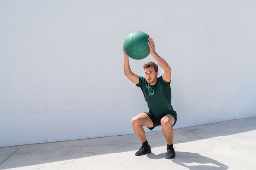 Squat with overhead medicine ball throw or shoulder press. Weight exercises workout fitness man training legs and glutes with weighted medicine ball squats. Athlete working out at gym.