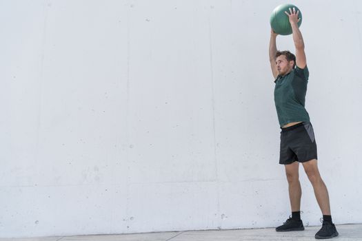 Fit man throwing medicine ball against gym floor upper body workout exercise. Cross training at fitness center.