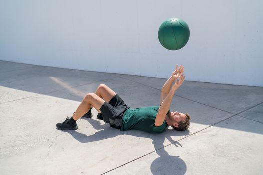 Strength training fit man cross training throwing medicine ball in the air for bench press arm workout exercises using heavy weight ball. Fitness athlete exercising on gym floor.