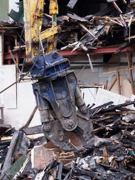 a demolition claw removing debris and rubble from a wrecked building damaged by fire