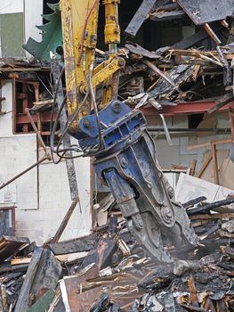 a large excavator demolition claw removing debris and rubble from a wrecked building destroyed by fire