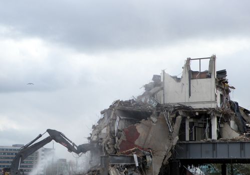 A digger working on a demolition site destroying a section of wall creating dust and rubble