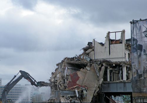 A digger working on a demolition site destroying a section of wall creating dust and rubble