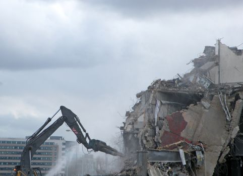 A digger working on a demolition site destroying a section of wall creating dust and rubble