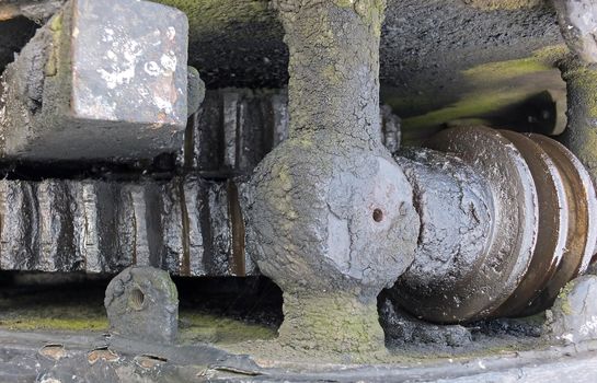 a close up of ancient greasy machinery with oily dirty gears and green moss growing on the metal