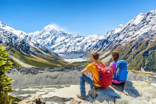 Backpackers couple hiking looking at Mount Cook view on mountains tramping in New Zealand. People hikers relaxing during hike in alps of south island.