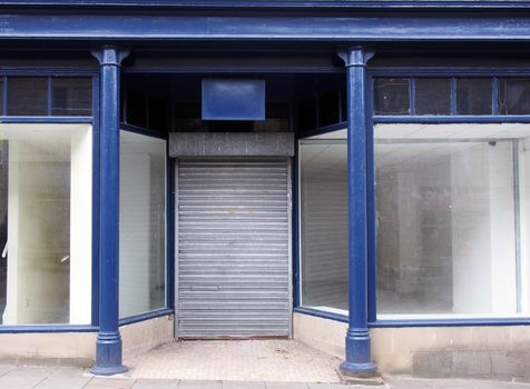 the facade of an old abandoned shop painted blue and white with empty store front dirty windows and closed shutters on the door