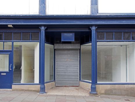 the facade of an old abandoned shop painted blue and white with empty store front dirty windows and closed shutters on the door