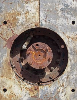 close up full frame detail of old rusting machinery with circular hole in steel plates with bolts and round drive shaft in the center in sunlight and shadow