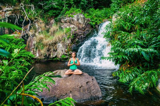 Yoga woman meditating at waterfall lush forest in Kauai, Hawaii. Spiritual woman praying namaste in tranquil serenity. Meditation in nature.