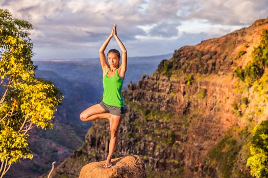 Yoga serene woman meditating doing tree pose Vriksasana on mountain nature landscape. Woman practicing meditation in sunset, healthy active lifestyle.